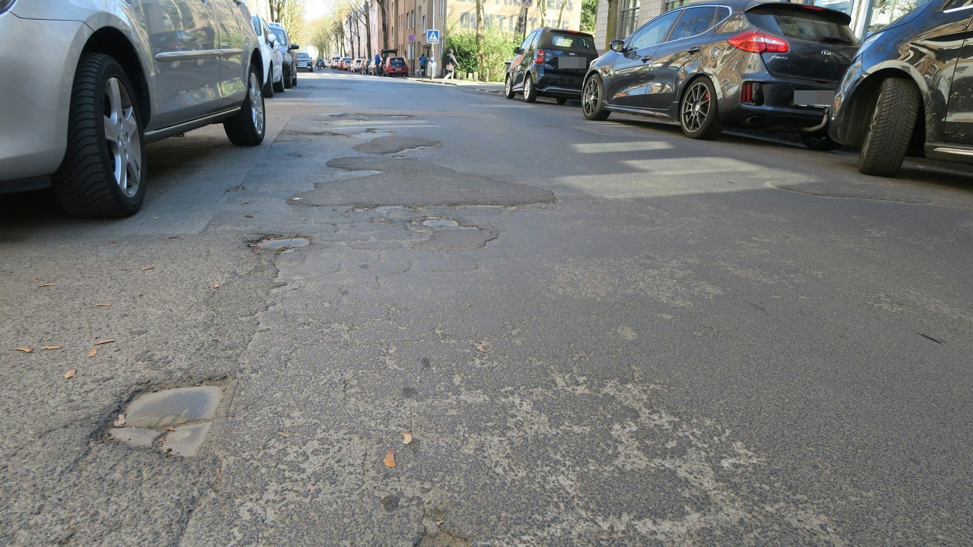 Aus der Froschperspektive aufgenommenes Bild, das die Löcher und Flicken im Asphalt einer Straße zeigt