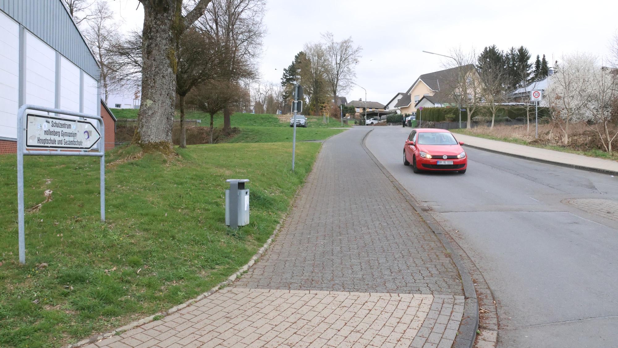 Blick auf eine Straße an einer Schule. Ein rotes Auto fährt auf der Straße.