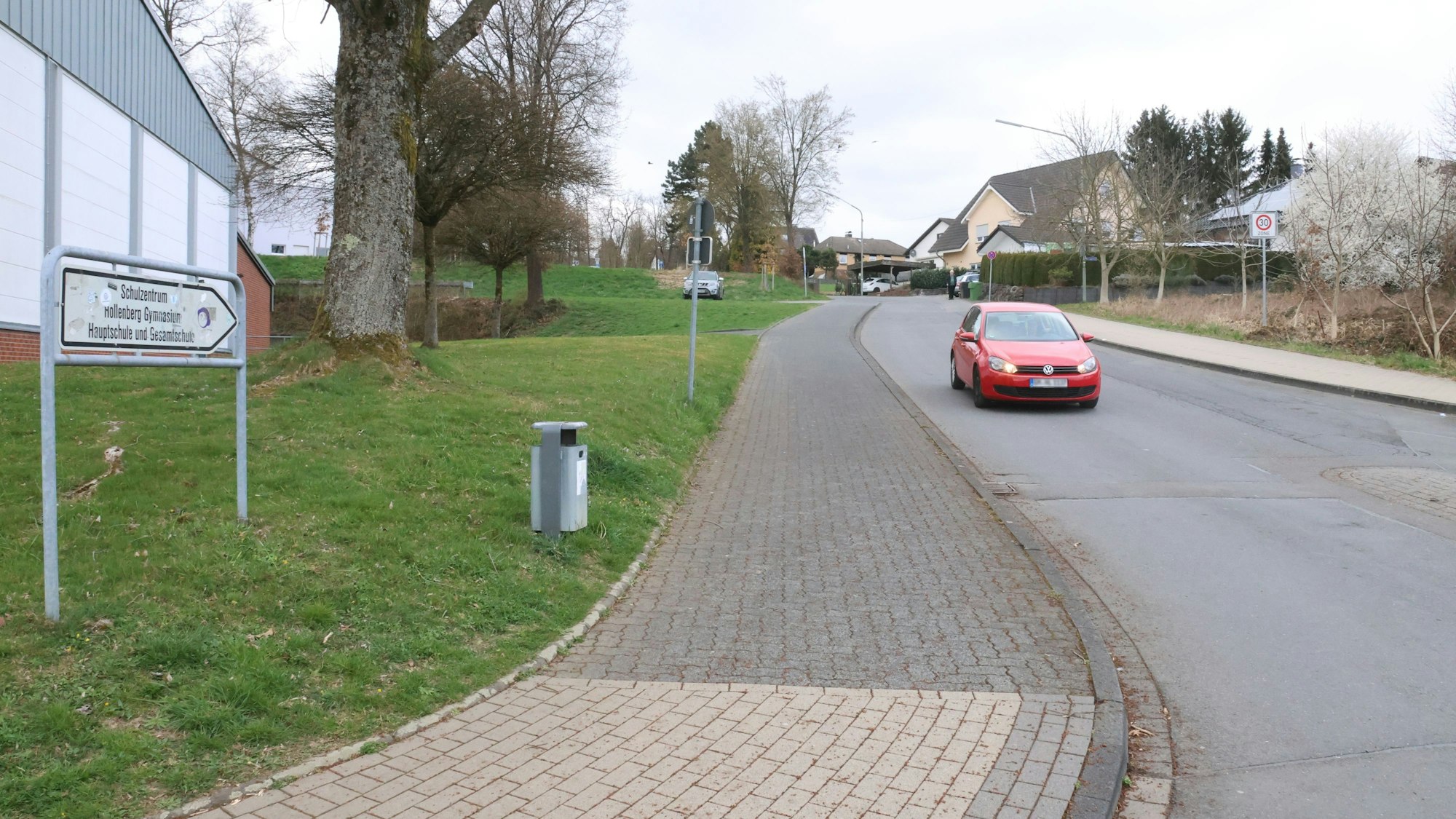 Blick auf eine Straße an einer Schule. Ein rotes Auto fährt auf der Straße.