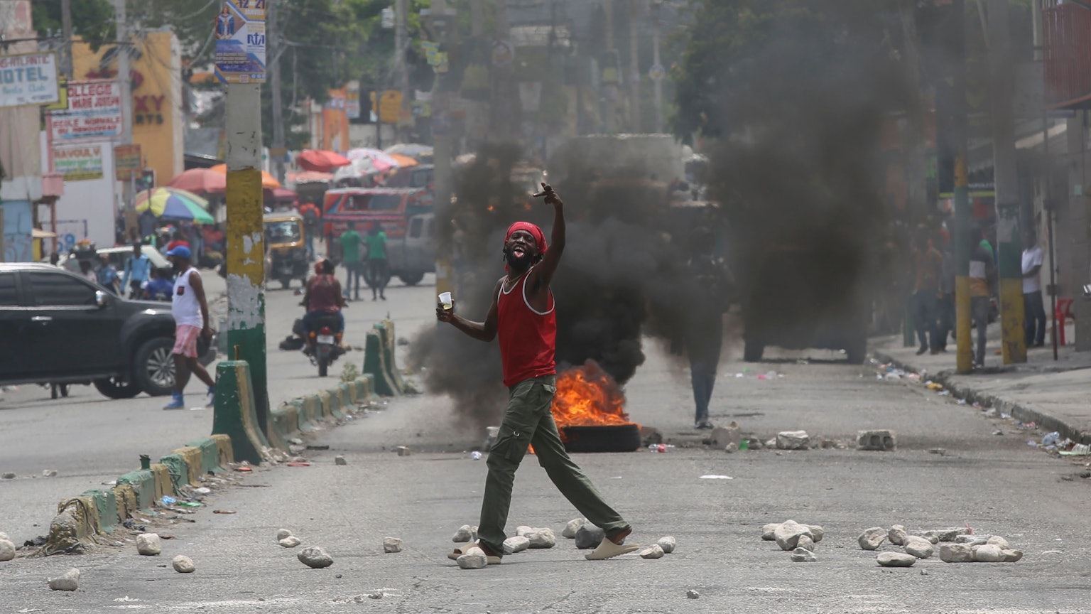 Ein Mann gestikuliert auf einer Straße, die durch brennende Reifen und Trümmer blockiert ist, während einer Demonstration, die den Rücktritt des Übergangspräsidentenrates fordert, in Port-au-Prince, Haiti.