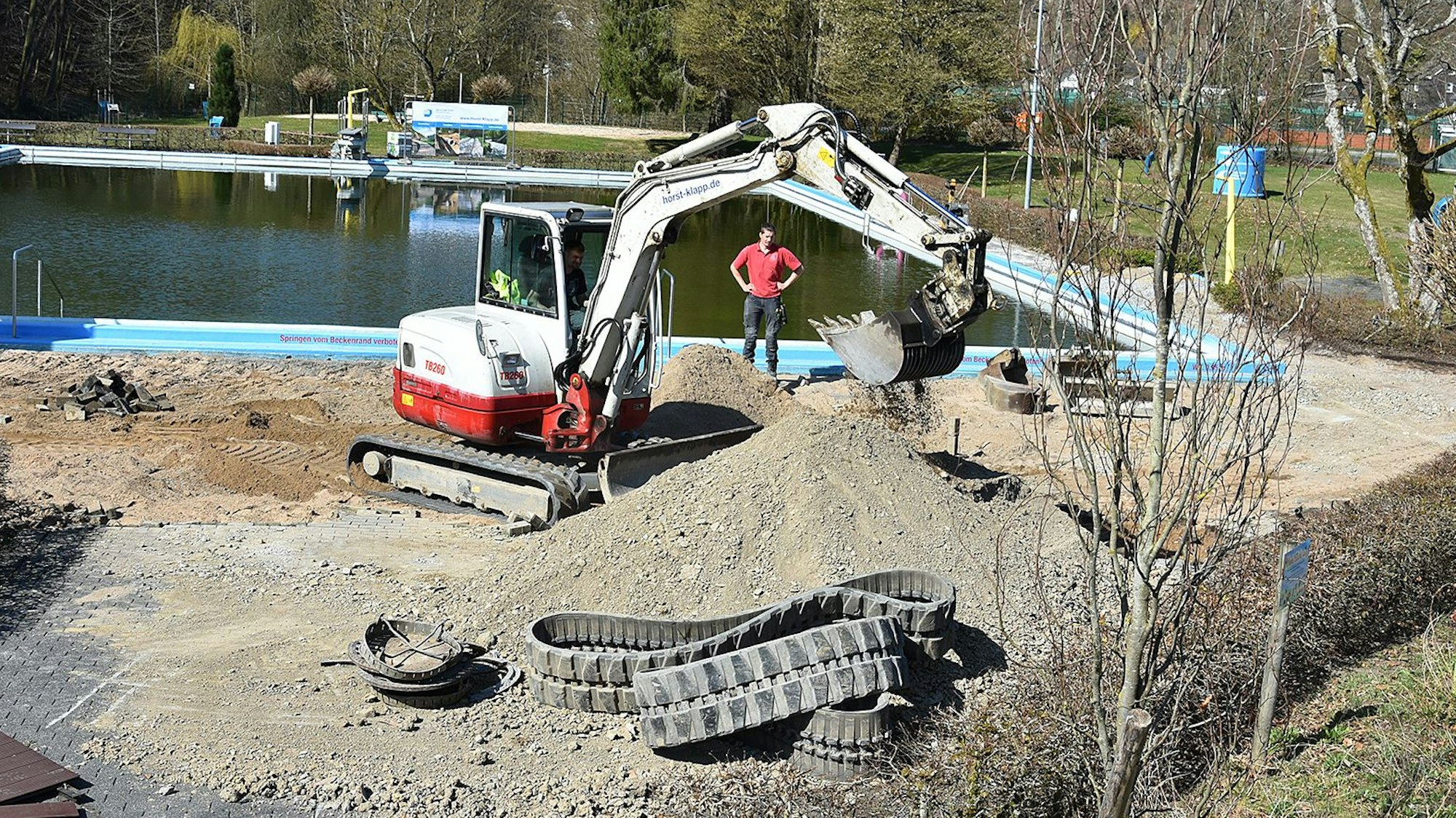Zu sehen sind Bauarbeiten mit einem Bagger in einem Freibad.