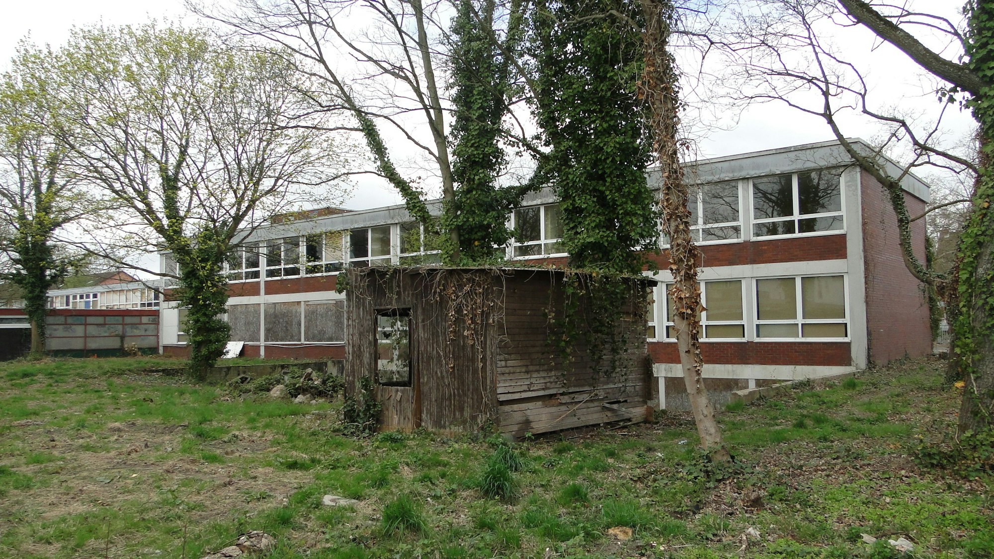 Ein schmuckloser zweistöckiger Bau ist von einer Wiese aus zu sehen.