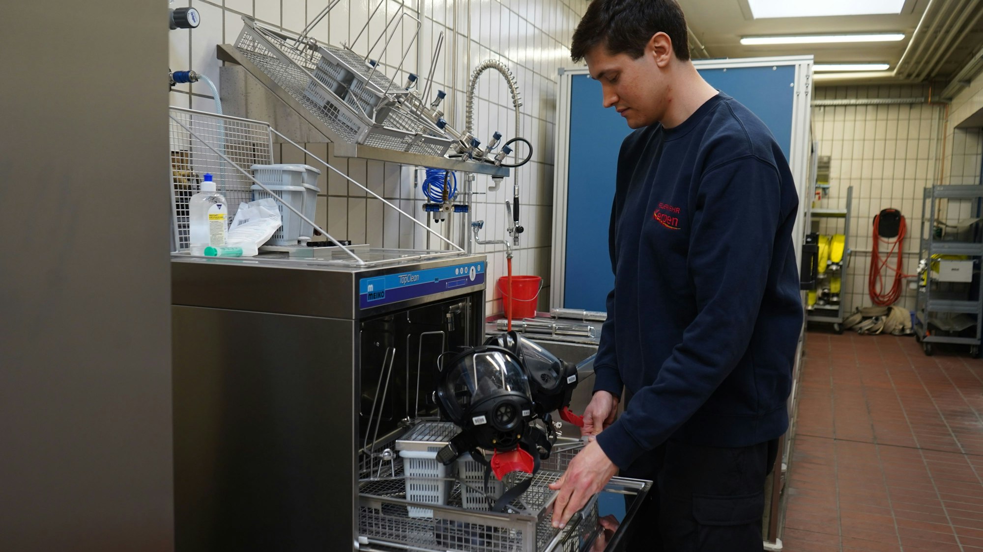 Das Foto zeigt einen jungen Mann, der Feuerwehr-Masken in ein Reinigungsgerät einräumt.