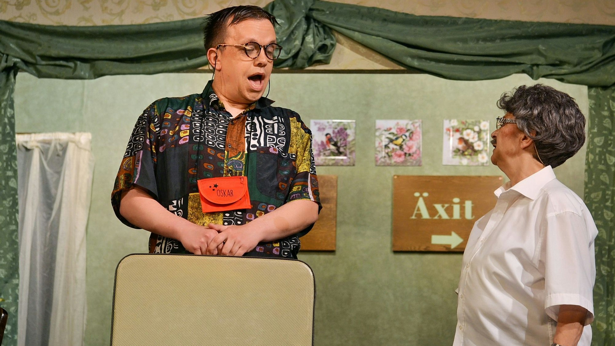 Zwei Laiendarsteller des Theatervereins Niederelvenich bei ihrem Auftritt. Einer trägt einen Reisekoffer in der Hand.