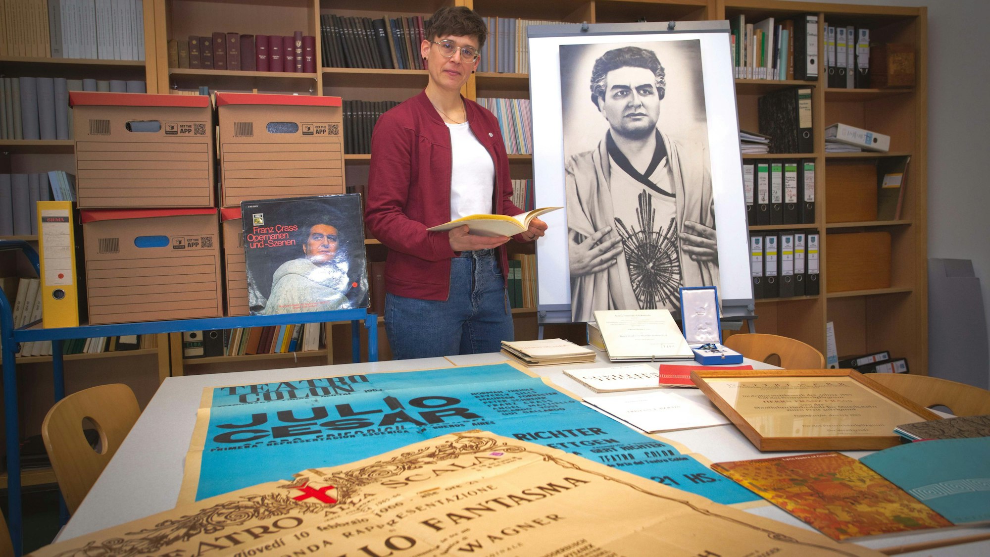 Das Foto zeigt Plakate, Urkunden und Fotos aus dem Nachlass des Opernsängers Franz Crass, dazwischen Stadtarchivarin Sarah Zeppenfeld.