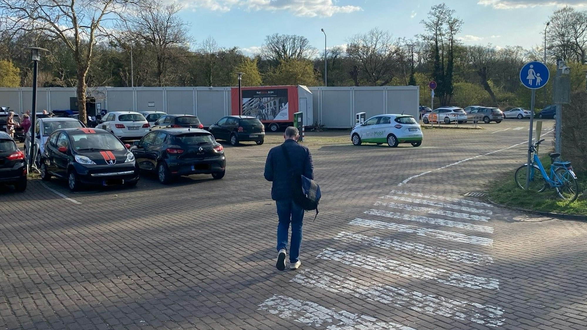 Zu sehen ist ein Mann, der über einen Parkplatz zur provisorischen Radstation geht.