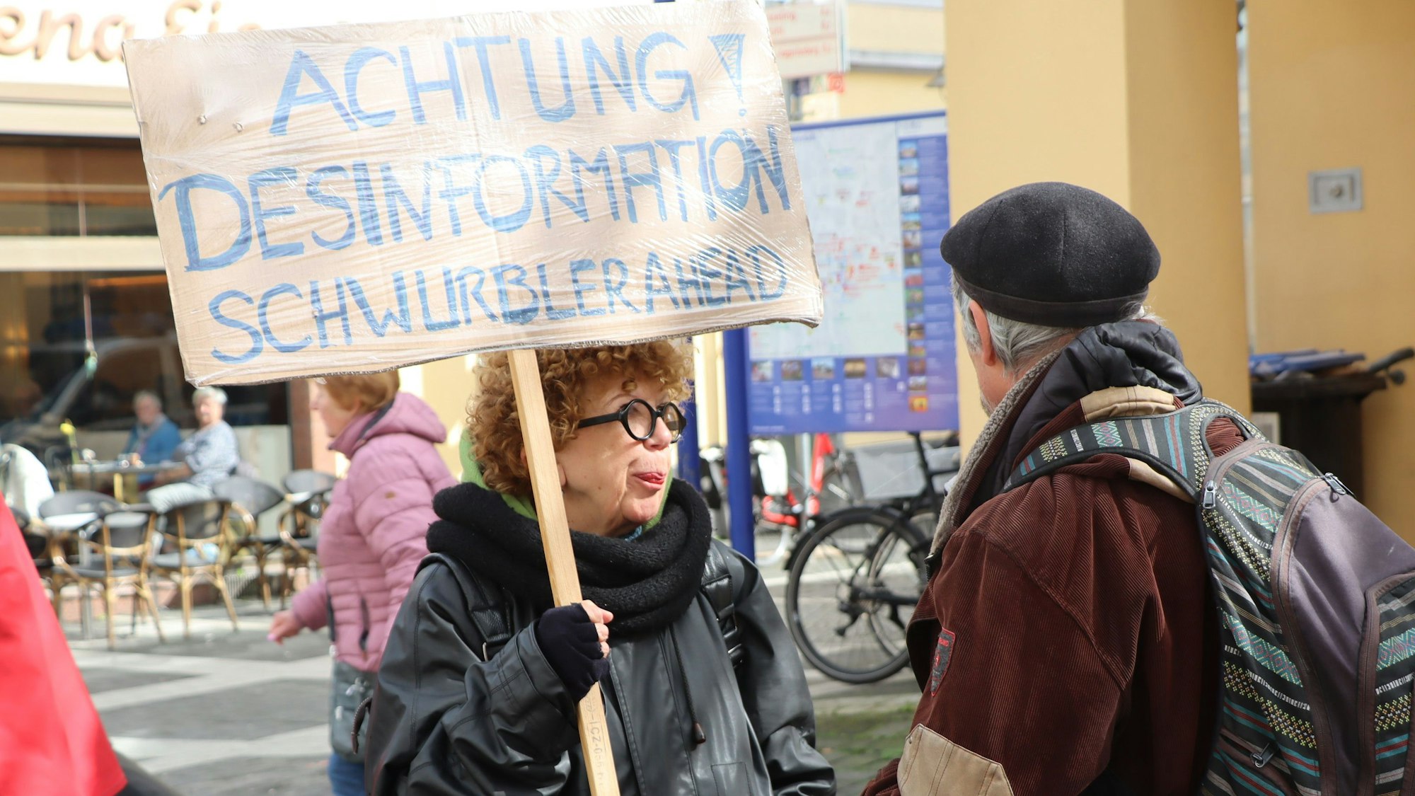 Auf dem Foto ist eine Frau zu sehen, die ein Plakat hochhält und mit einem Mann diskutiert.