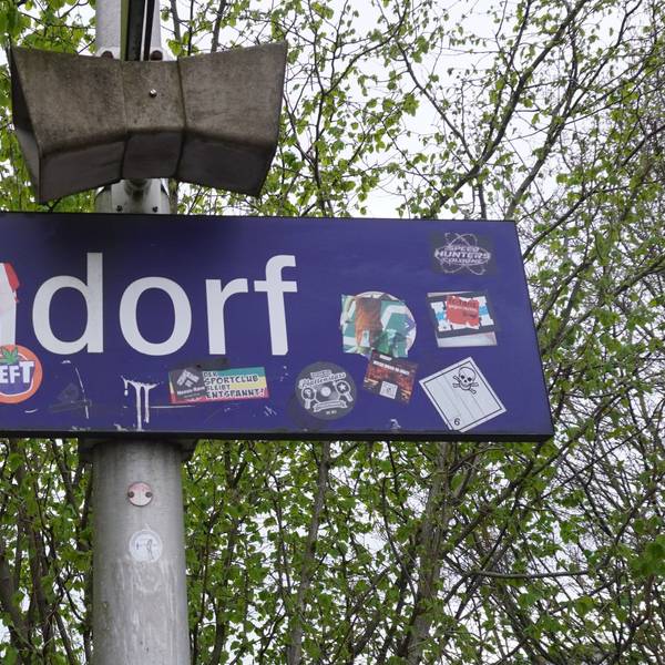 Das Foto zeigt ein Bahnhofsschild mit der Aufschrift „Sindorf“, die teils überklebt ist.