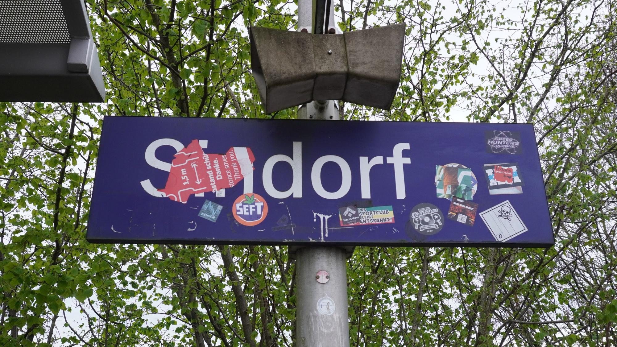 Das Foto zeigt ein beklebtes Bahnhofsschild mit der Aufschrift „Sindorf“.