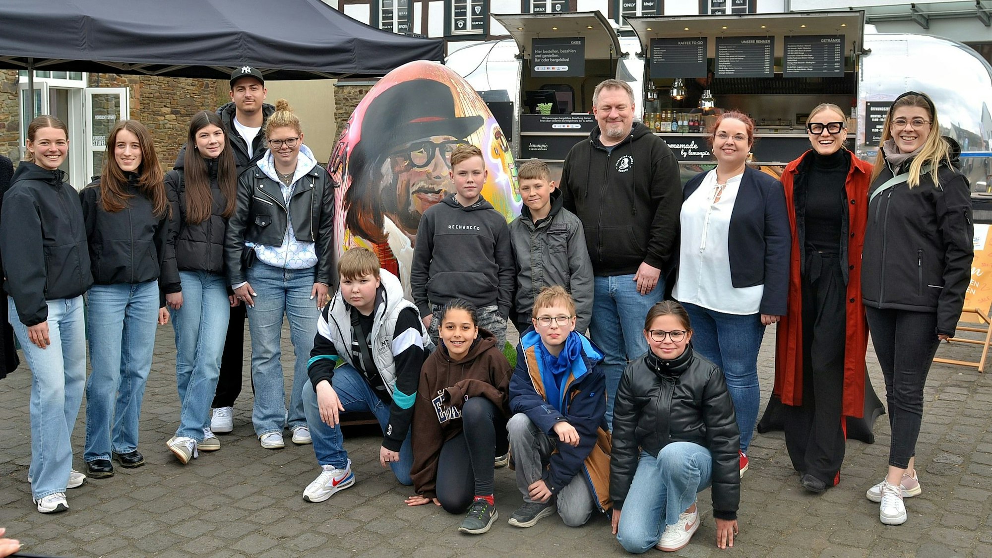 Schülerinnen und Schüler haben sich vor einem Kunst-Ei aufgestellt.