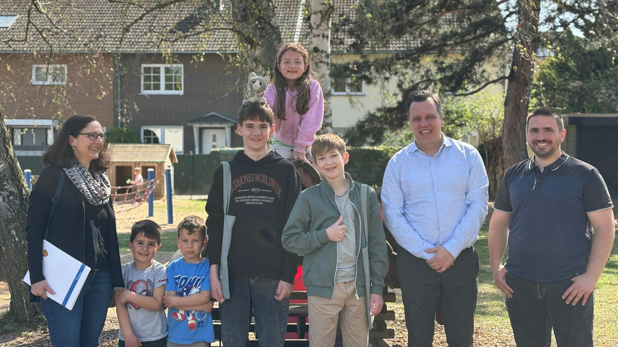 Kinder, Jugendliche und Erwachsene posieren draußen an einem Spielplatz.