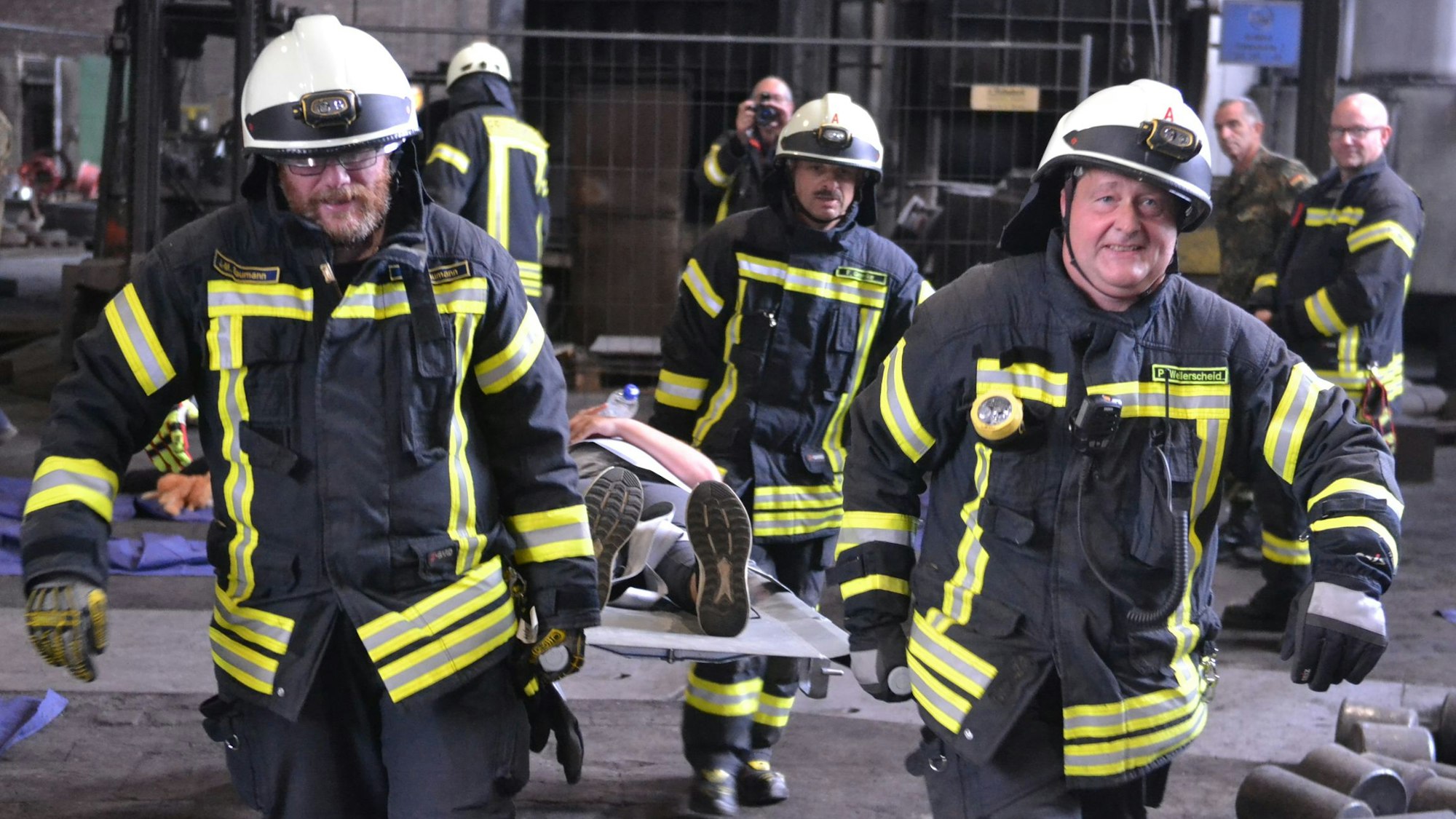 Im Rahmen einer Übung tragen vier Feuerwehrleute einen Verletztendarsteller auf einer grauen Krankentrage.