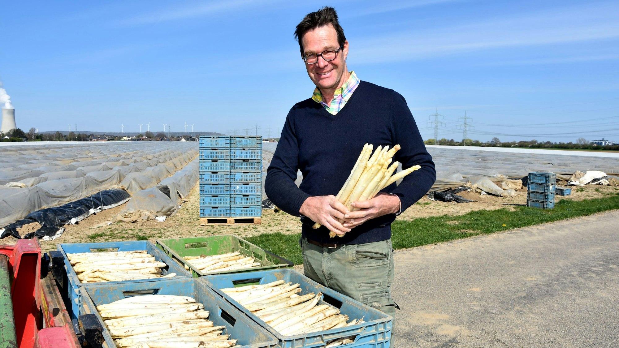 Ein Mann steht vor einem Feld und hält Spargel in den Händen.