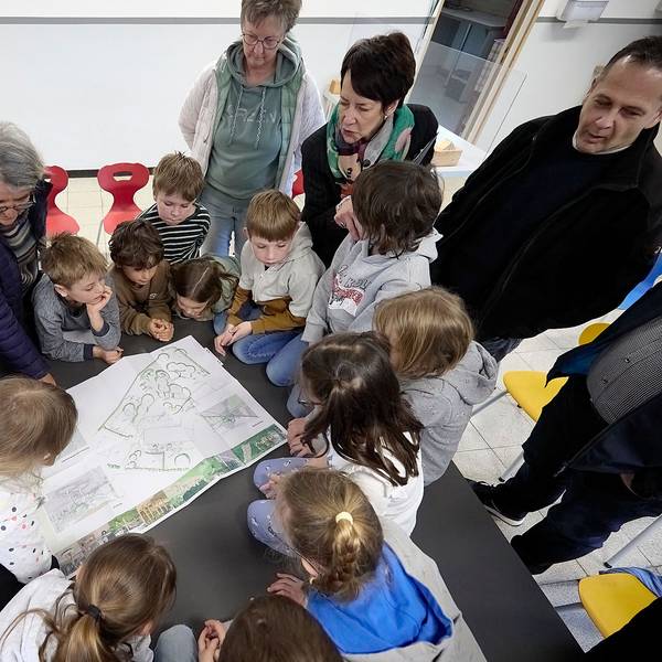 Zahlreiche Kinder und eine Frau schauen auf einen Plan für den neuen Schulhof in Nettersheim-Marmagen.