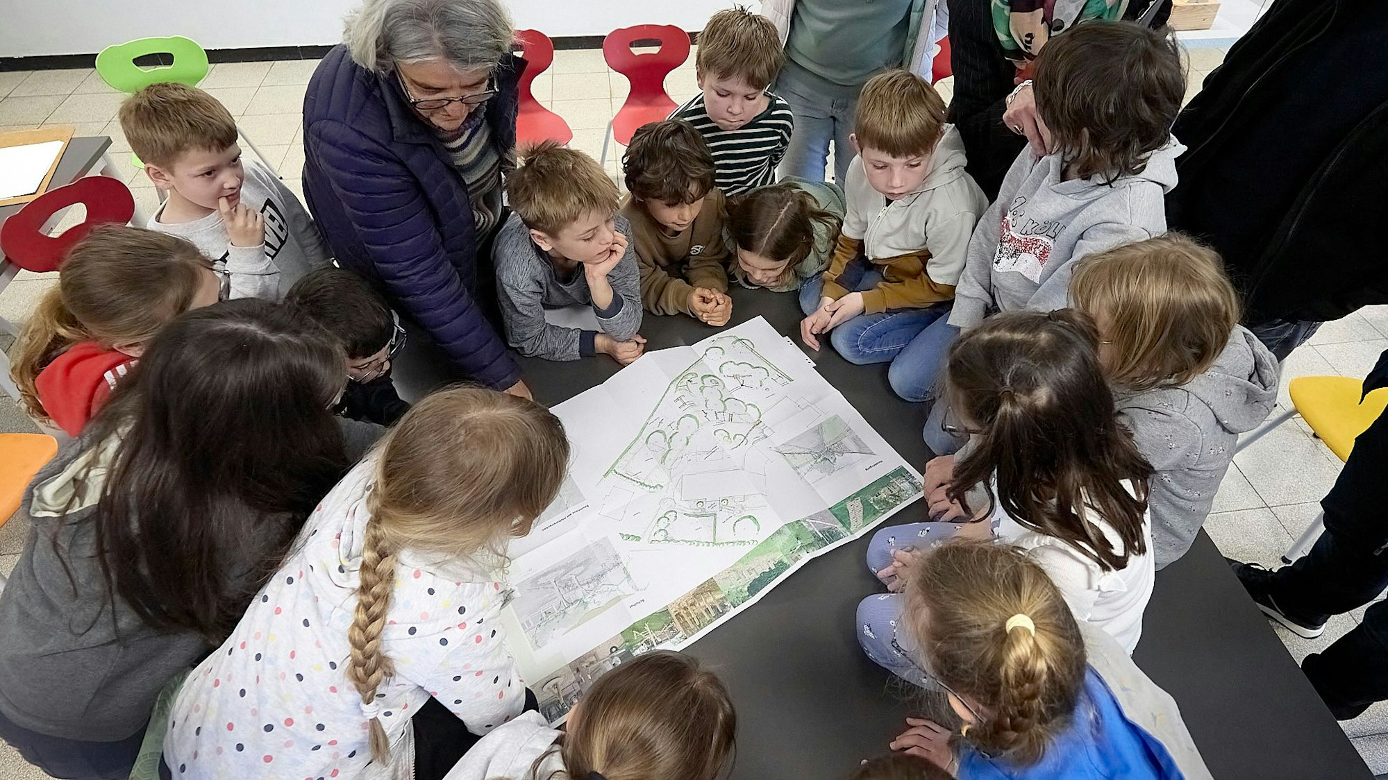 Zahlreiche Kinder und eine Frau schauen auf einen Plan für den neuen Schulhof in Nettersheim-Marmagen.