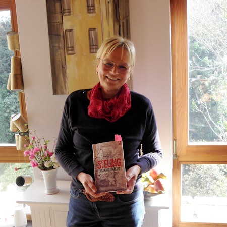 Die Autorin Ute Mainz hält ihr neues Buch in den Händen. Mit pinkfarbenen Zetteln sind einige Stellen markiert, die sie bei ihren Lesungen vortragen will.