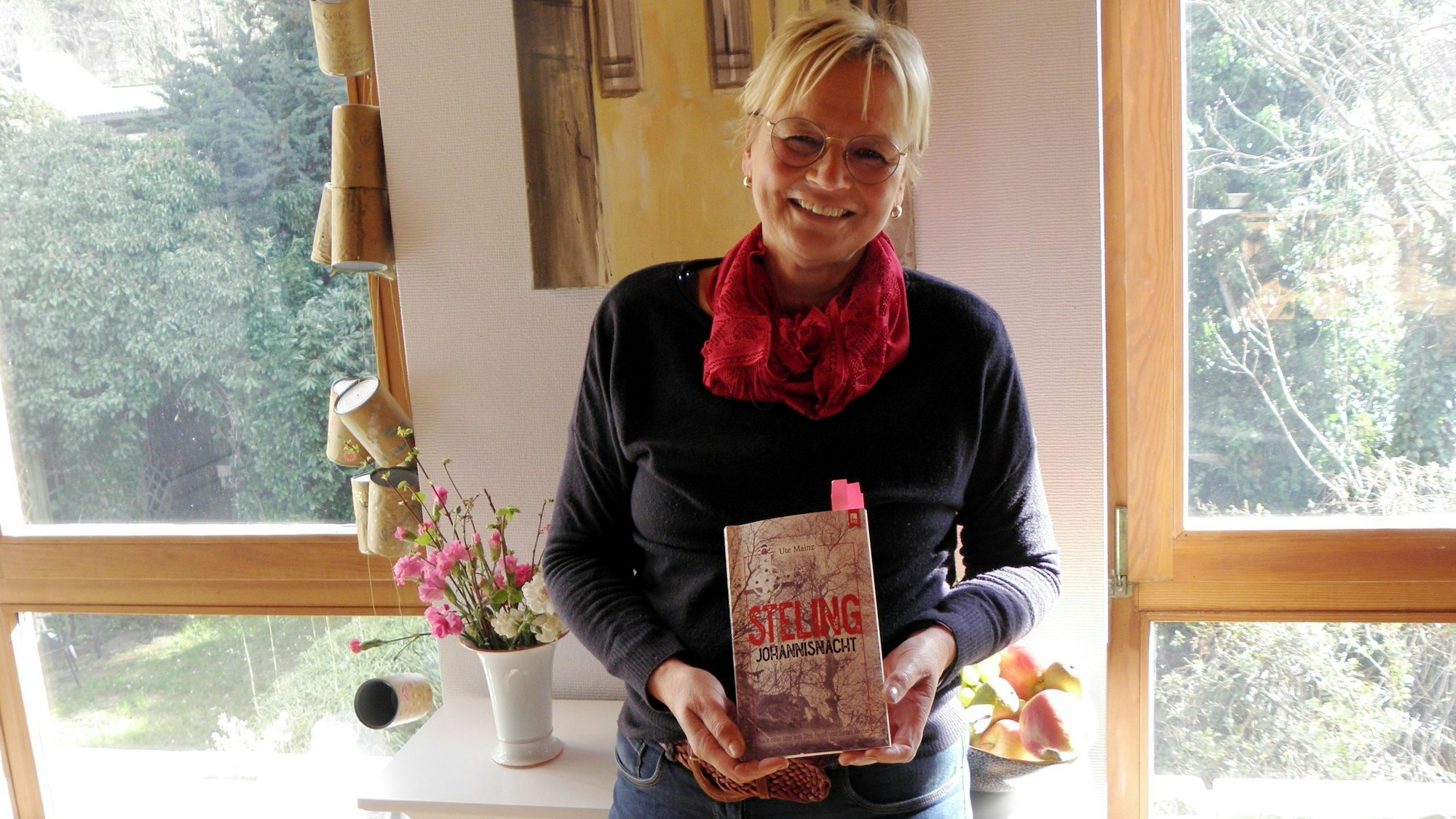 Die Autorin Ute Mainz hält ihr neues Buch in den Händen. Mit pinkfarbenen Zetteln sind einige Stellen markiert, die sie bei ihren Lesungen vortragen will.