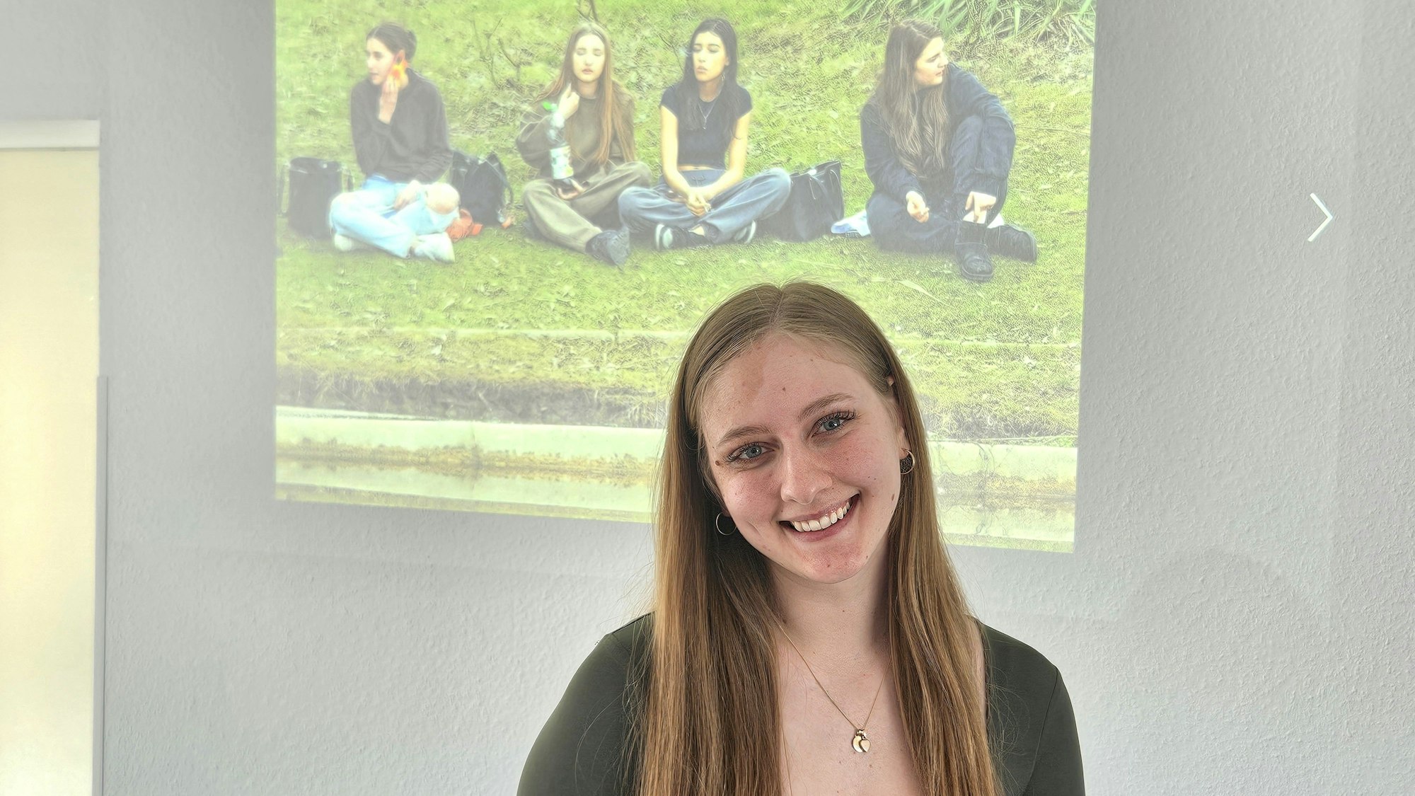 Nancy Bormann steht vor einem an die Wand projiziertes Foto mit Mädchen, die am Boden sitzen.