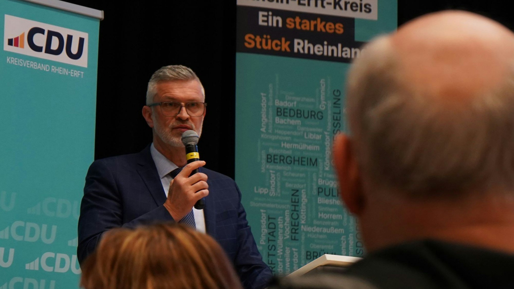 Auf dem Foto ist Harald Stingl im Anzug zu sehen, der in ein Mikrofon spricht.