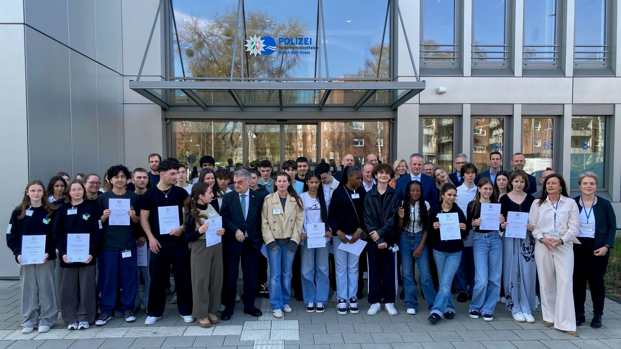 Das Bild zeigt rund 40 Schülerinnen und Schüler mit Innenminister Herbert Reul vor dem Polizeigebäude in Bergheim.