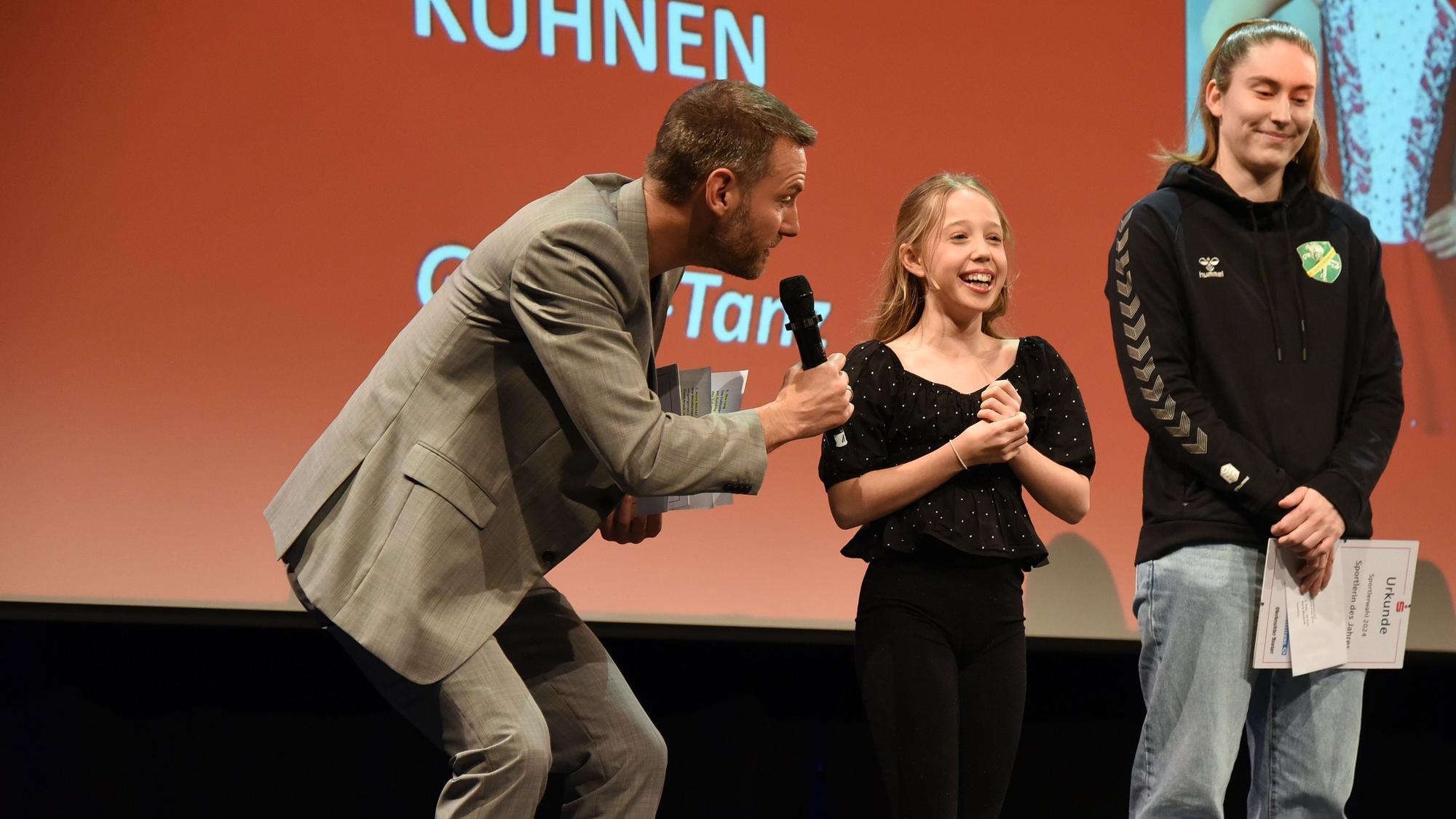 Zu sehen ist ein Moderator, der ein zwölfjähriges Mädchen interviewt.