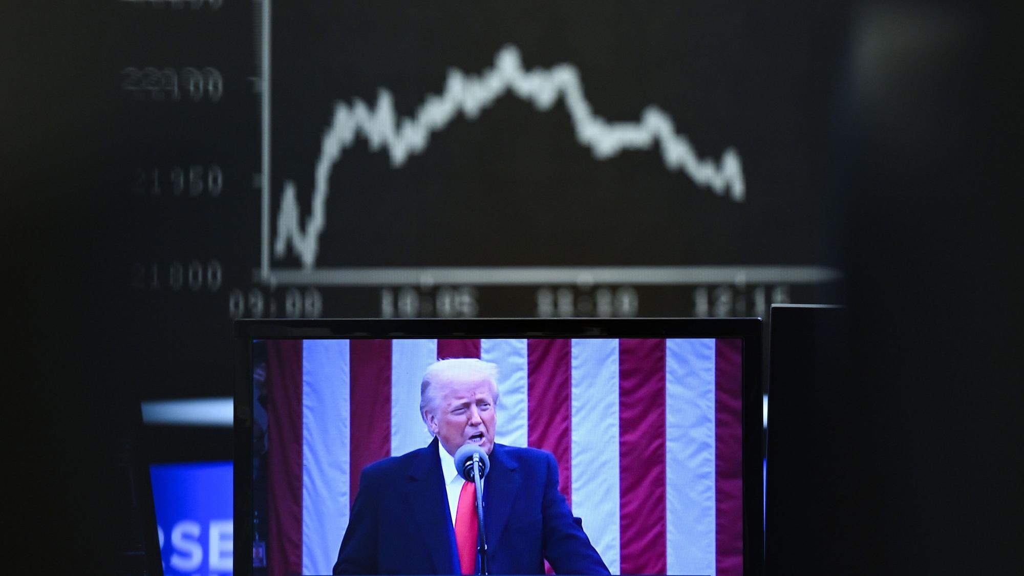 Hinter einem Fernsehmonitor, auf dem US-Präsident Donald Trump zu sehen ist, zeigt die Anzeigetafel mit der Dax-Kurve fallende Kurse