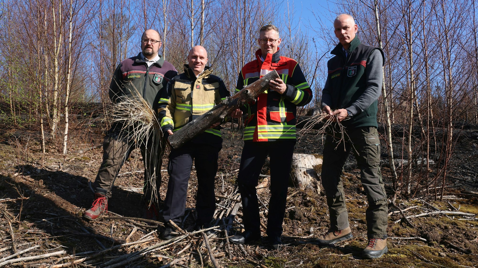 Vier Männer stehen im Wald und halten trockenes Holz in den Händen.
