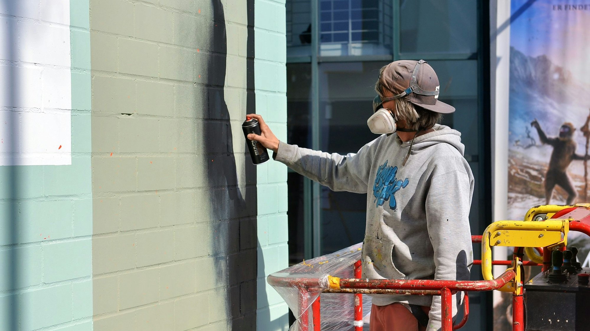 Kai Niederhausen, mit Mundschutz, Brille und Kappe, sprüht Farbe aus einer Dose auf die Fassade.