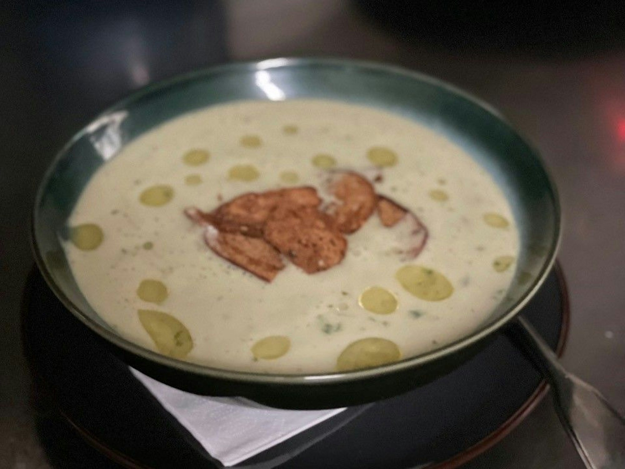 Zu sehen ist ein Teller Bärlauchsuppe mit Zitronenöl und Brotchips.