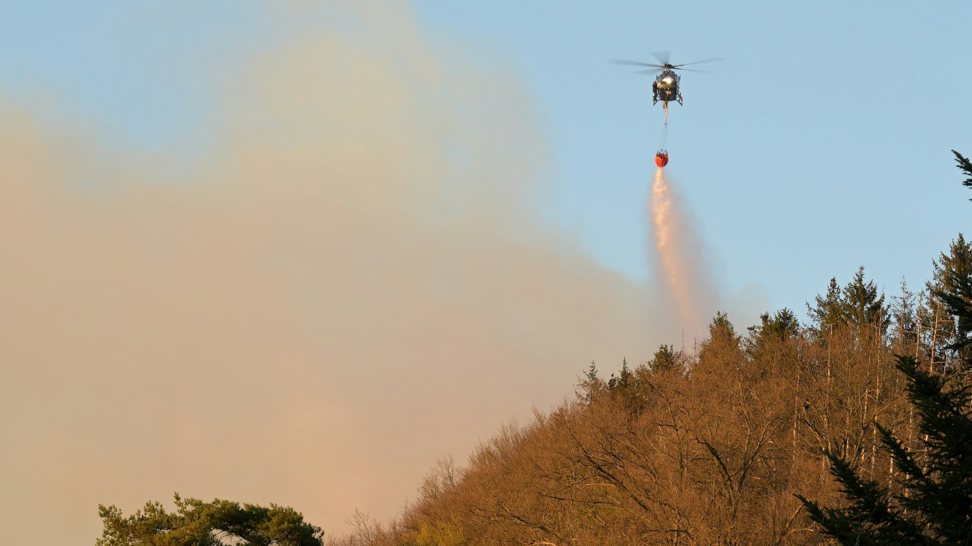 Ein Hubschrauber wirft Wasser über dem Brand ab.