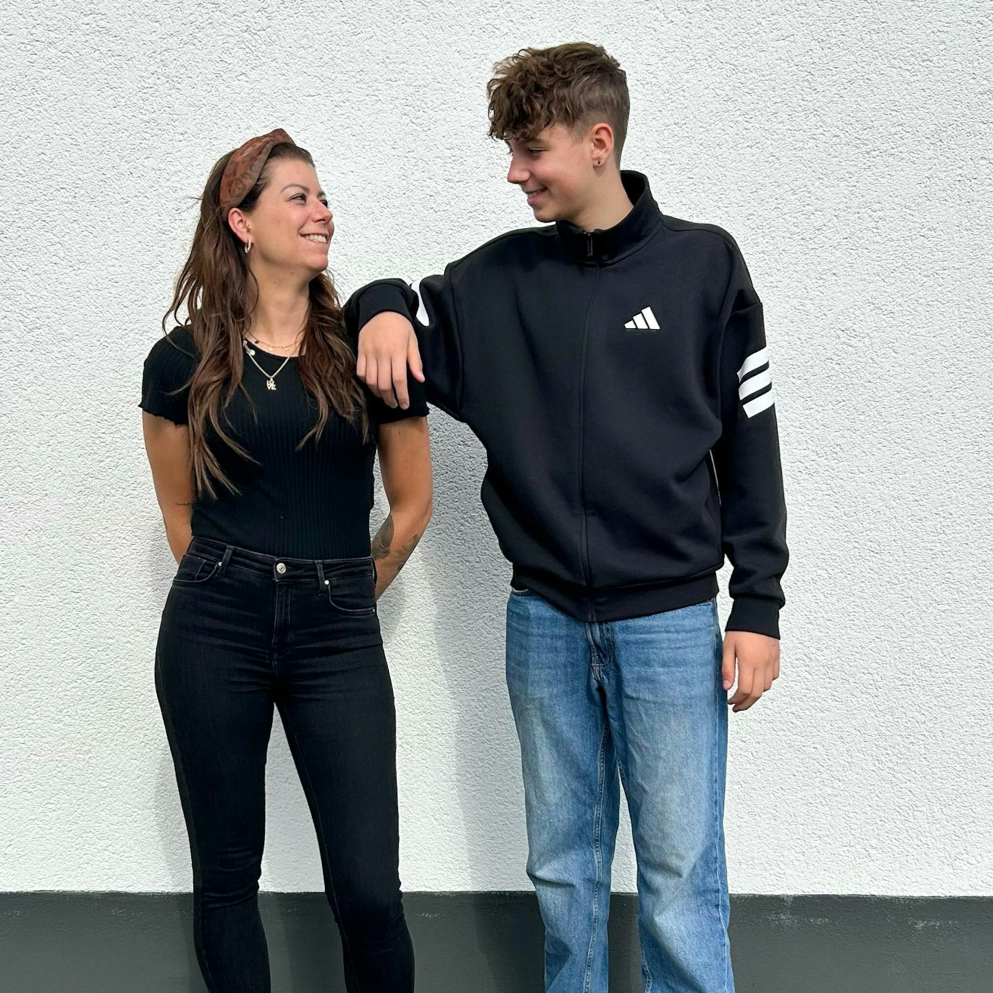 Der 13-jährige Matts Gross steht neben seiner Mutter Nici vor einer weißen Hauswand, die beiden lächeln sich an.