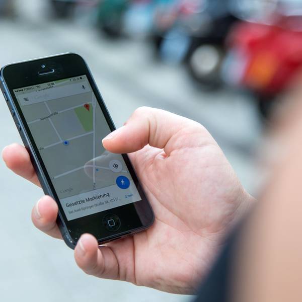 Eine Person schaut auf einem Parkplatz auf ihr Smartphone, auf dem die App Google Maps geöffnet ist