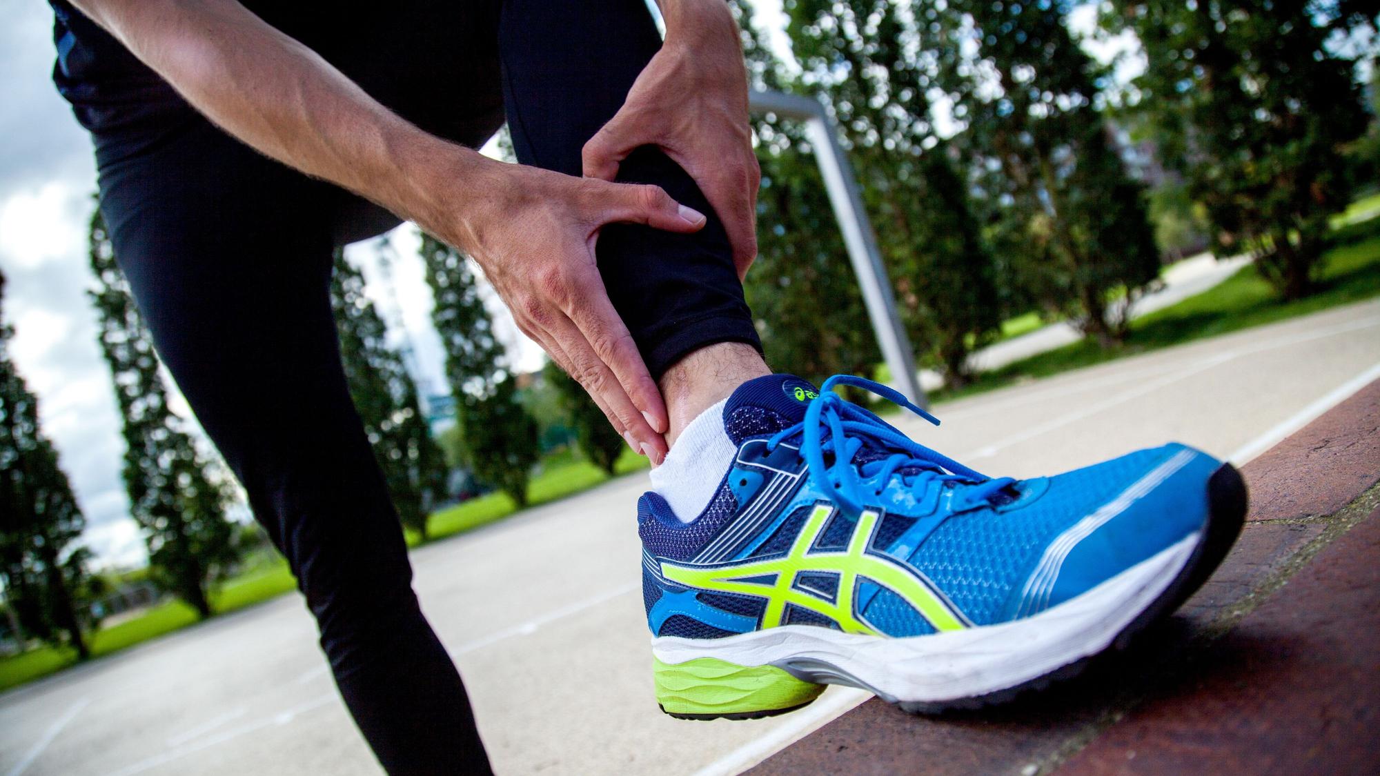 Eine sportlich angezogene Person in Laufschuhen hält sich den unteren Bereich der Wade