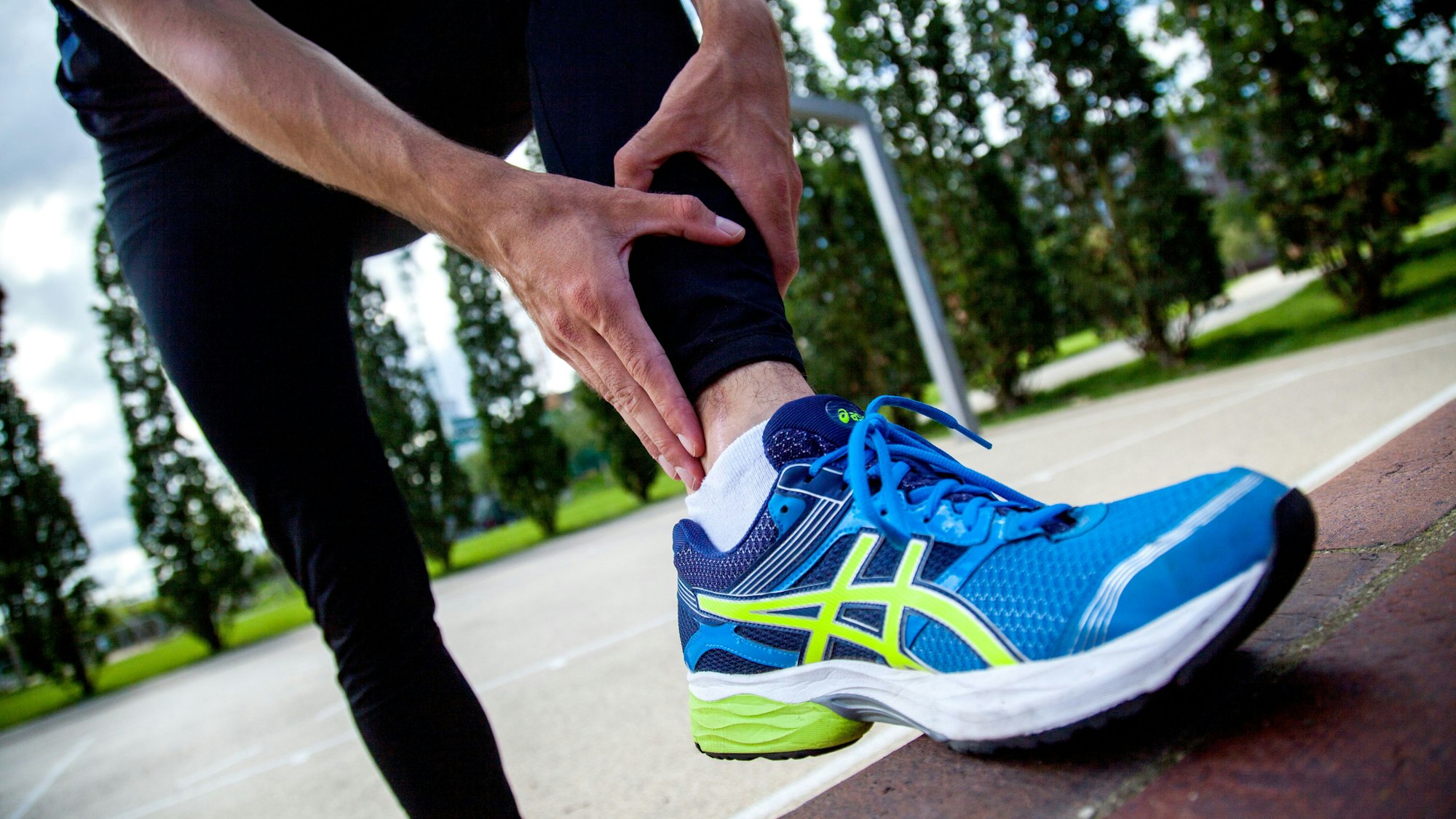 Eine sportlich angezogene Person in Laufschuhen hält sich den unteren Bereich der Wade