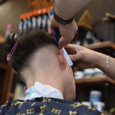 Ein Friseur rasiert in einem Barbershop die Haare eines männlichen Kunden.