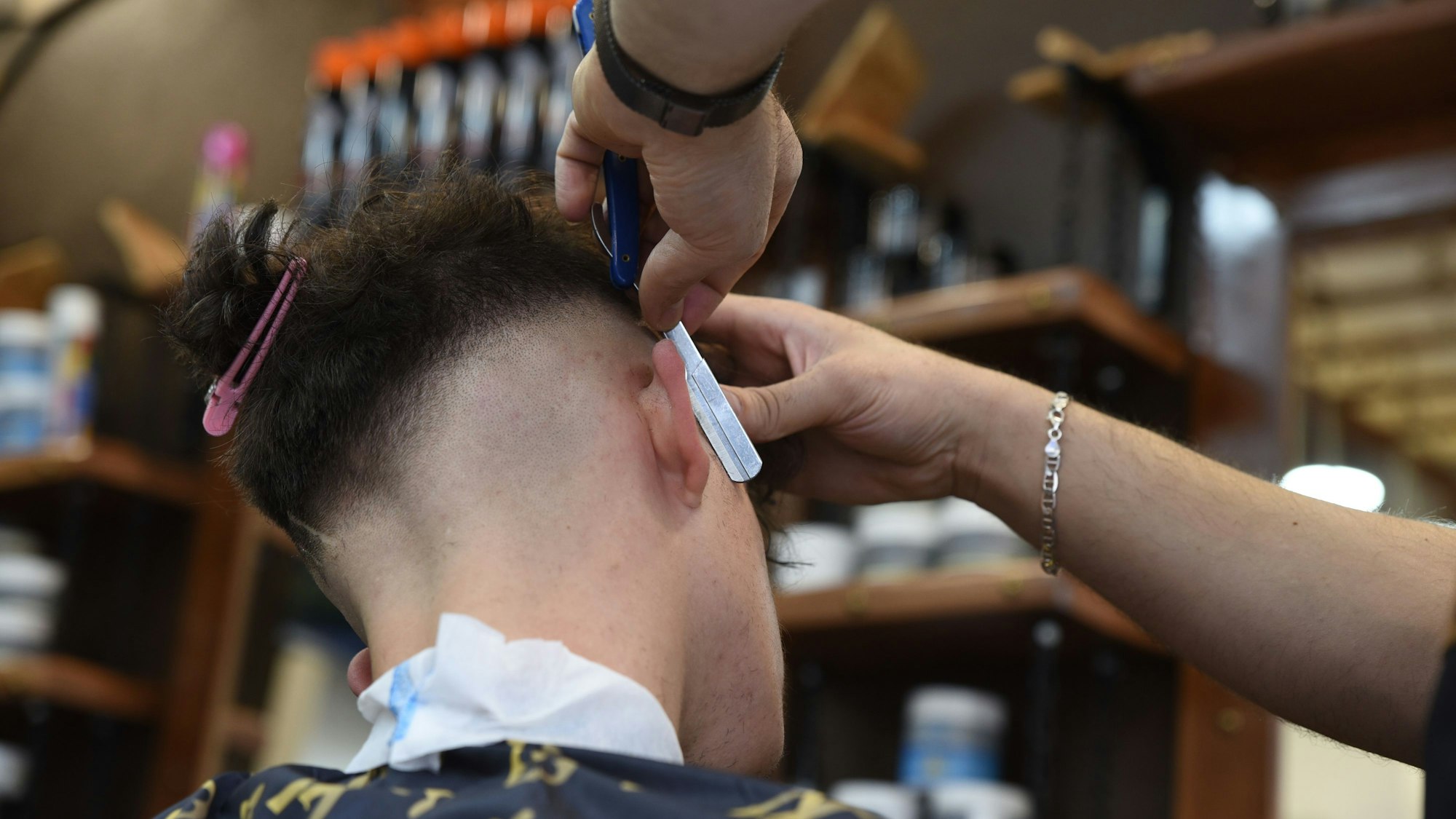 Ein Friseur rasiert in einem Barbershop die Haare eines männlichen Kunden.