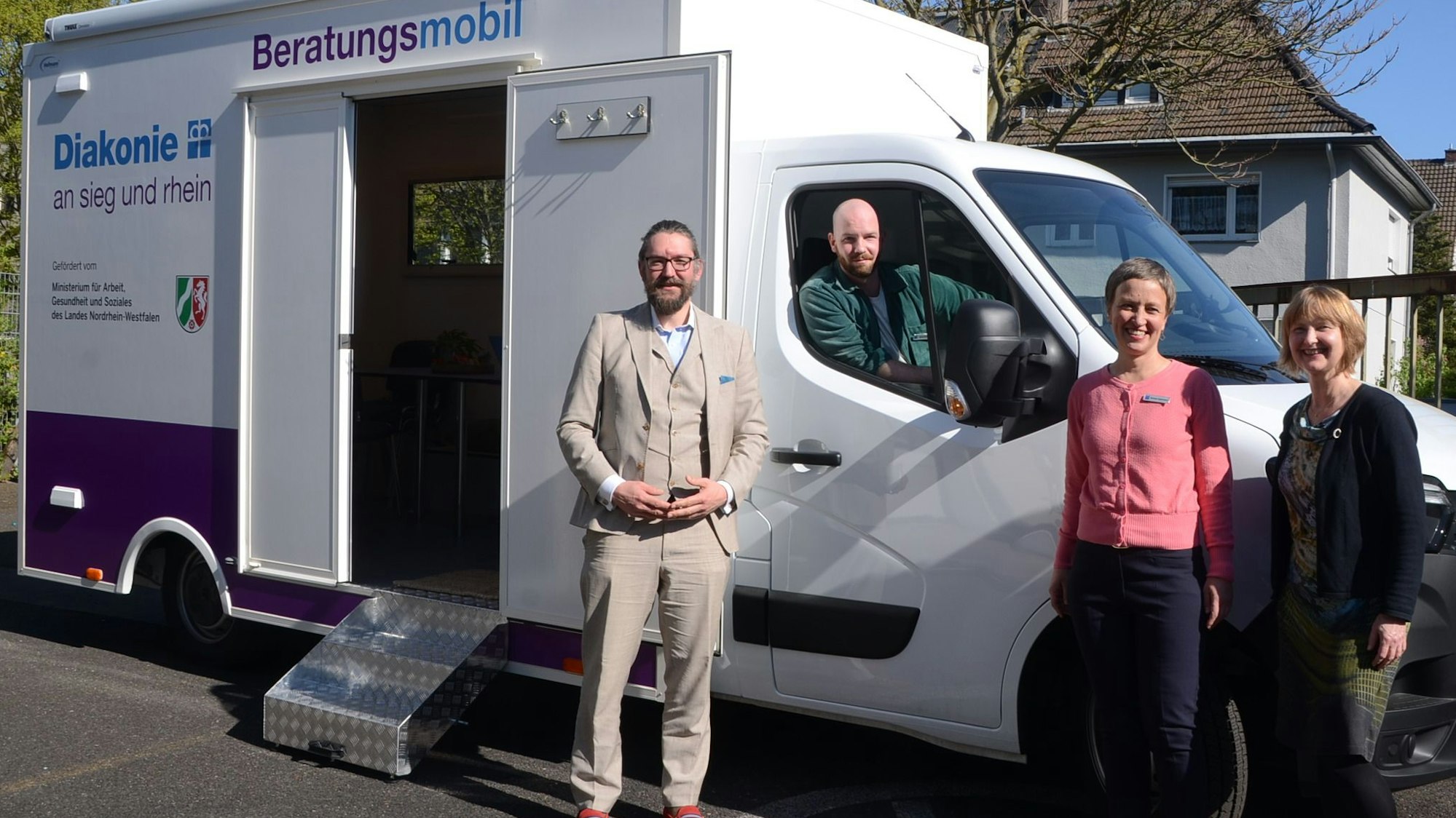 Zwei Frauen und ein Mann stehen vor einem Kleinlaster mit einem Containeraufbau, ein zweiter Mann sitzt im Führerhaus. Auf dem Aufbau steht Diakonie Beratungsmobil.