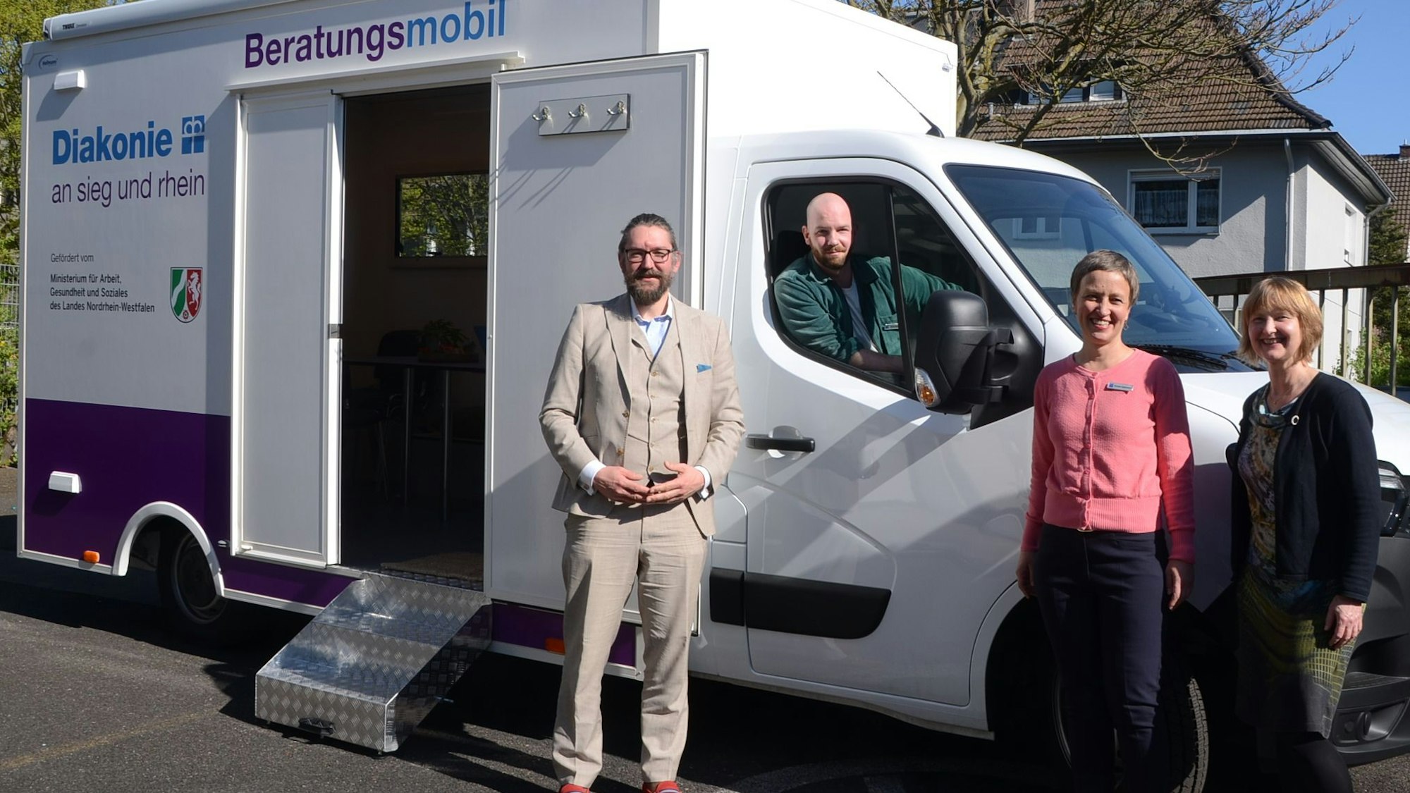 Zwei Frauen und ein Mann stehen vor einem Kleinlaster mit einem Containeraufbau, ein zweiter Mann sitzt im Führerhaus. Auf dem Aufbau steht Diakonie Beratungsmobil.