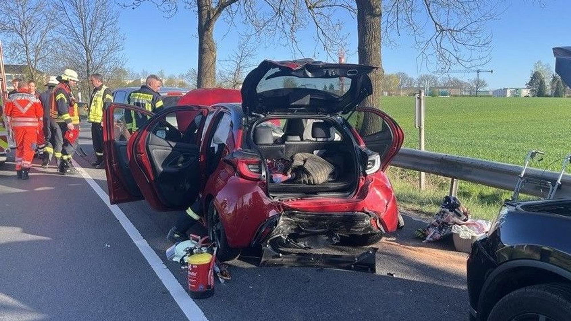 Ein beschädigter Kleinwagen an einer Unfallstelle; daneben stehen Einsatzkräfte von Rettungsdienst, Polizei und Feuerwehr.