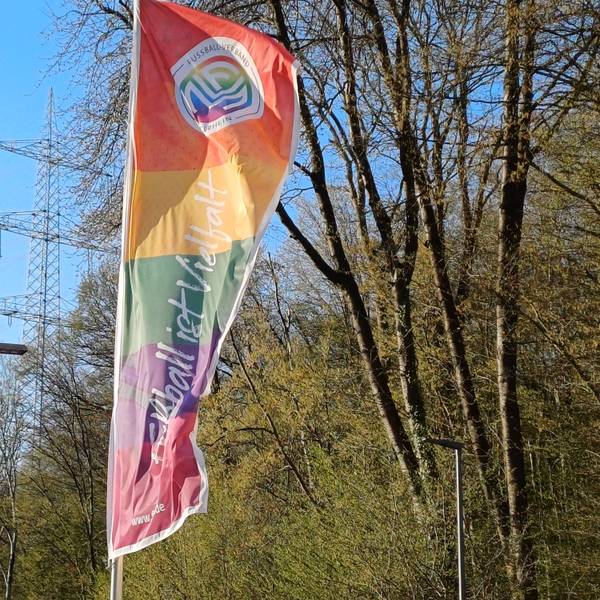Auf einer Flagge des Fußball-Verbands Mittelrhein im Regenbogenmuster steht „Fußball ist Vielfalt“.