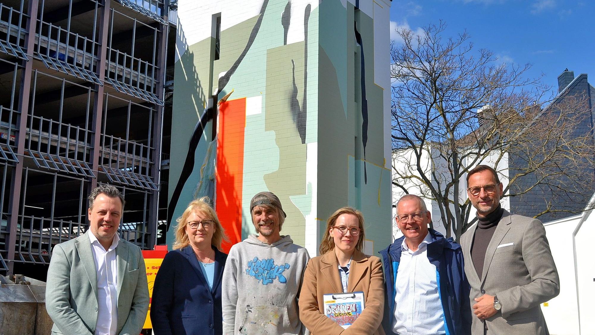 Zwei Frauen und vier Männer stehen in einer Reihe vor dem Parkhaus mit dem künstlerisch gestalteten Treppenhausturm.
