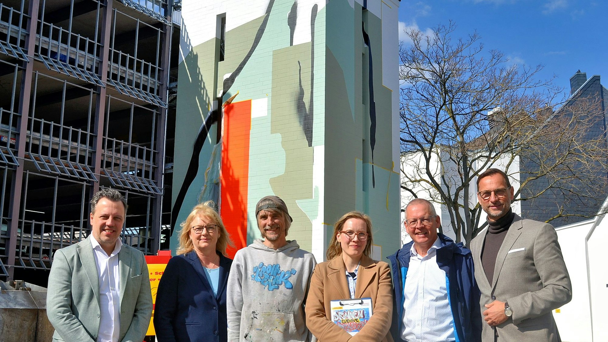 Zwei Frauen und vier Männer stehen in einer Reihe vor dem Parkhaus mit dem künstlerisch gestalteten Treppenhausturm.