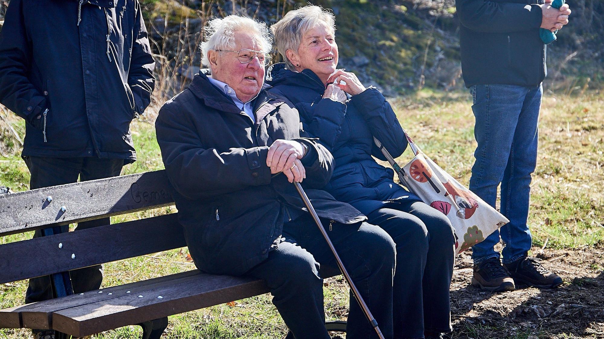 Rita Schumacher und Alois Sommer sitzen zusammen auf einer Bank im Freien.