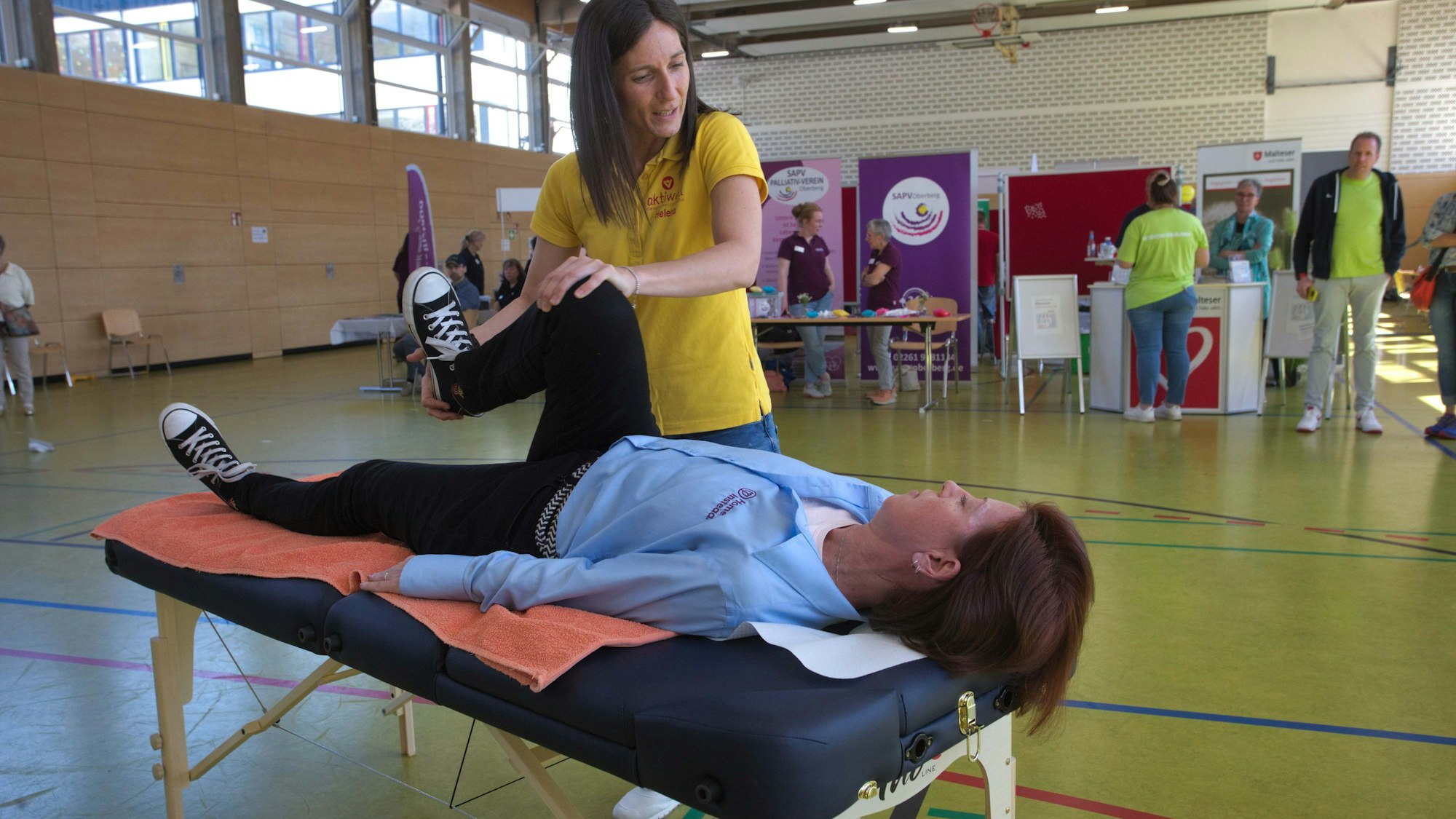 Eine Frau beugt das Knie einer vor ihr auf einer Liege gebetteten Frau.