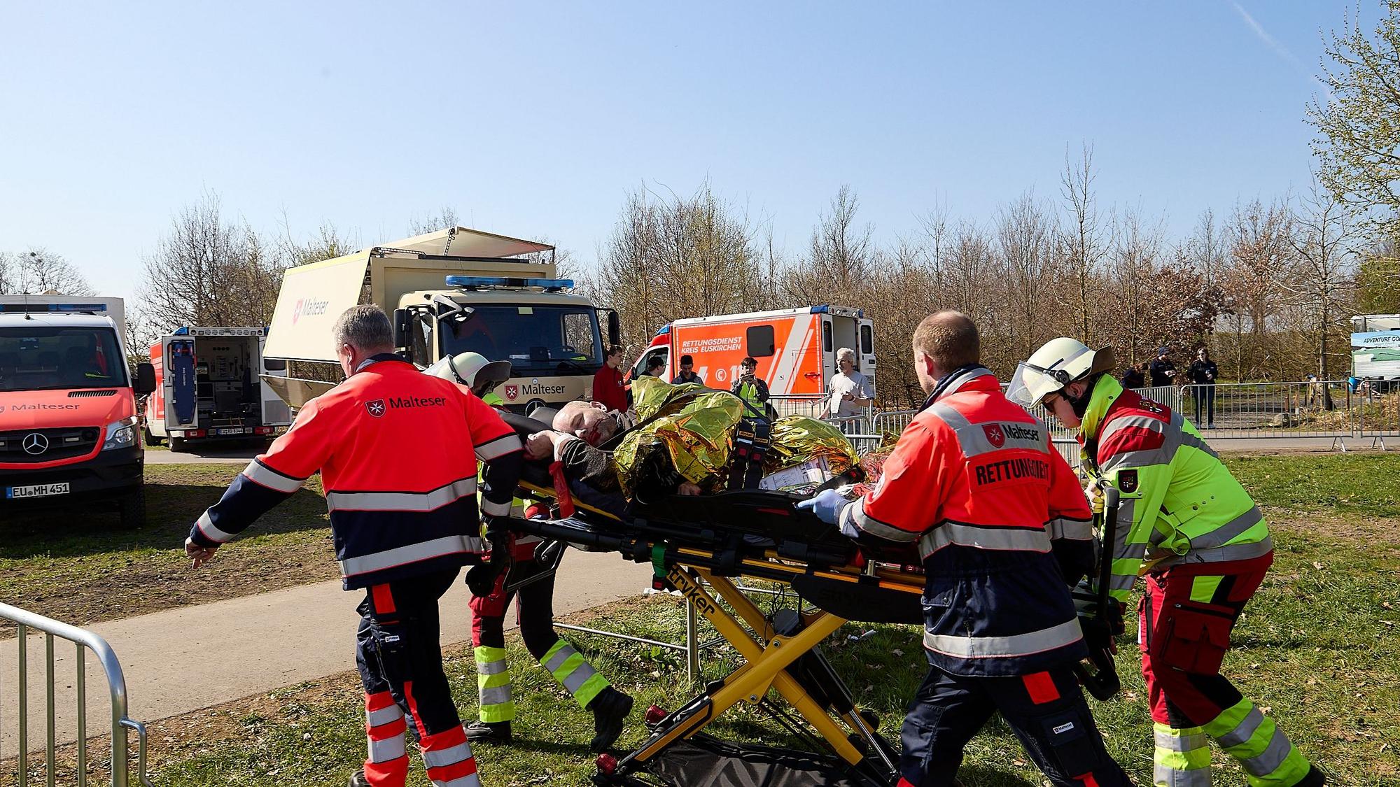 Vier Rettungskräfte transportieren einen Mann auf einer Krankentrage zu einem Rettungswagen.