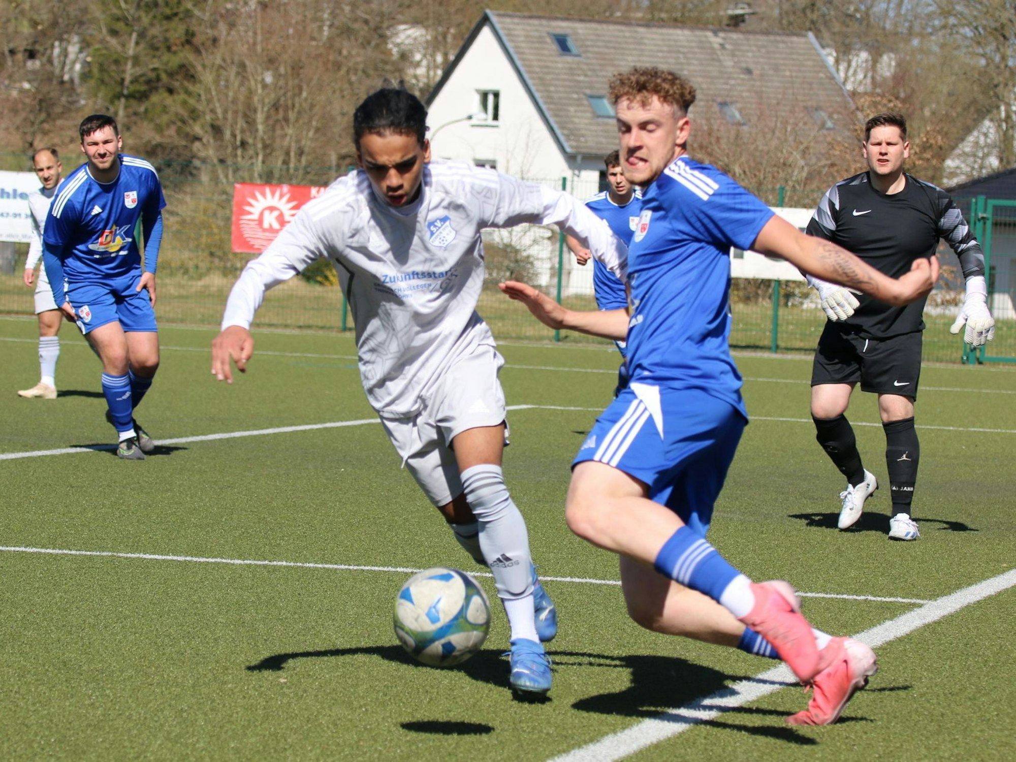 Zweikampf zwischen zwei Fußballer.Einer steht zwar außerhalb des Spielfeldes, kann die Situation aber beherzt klären.