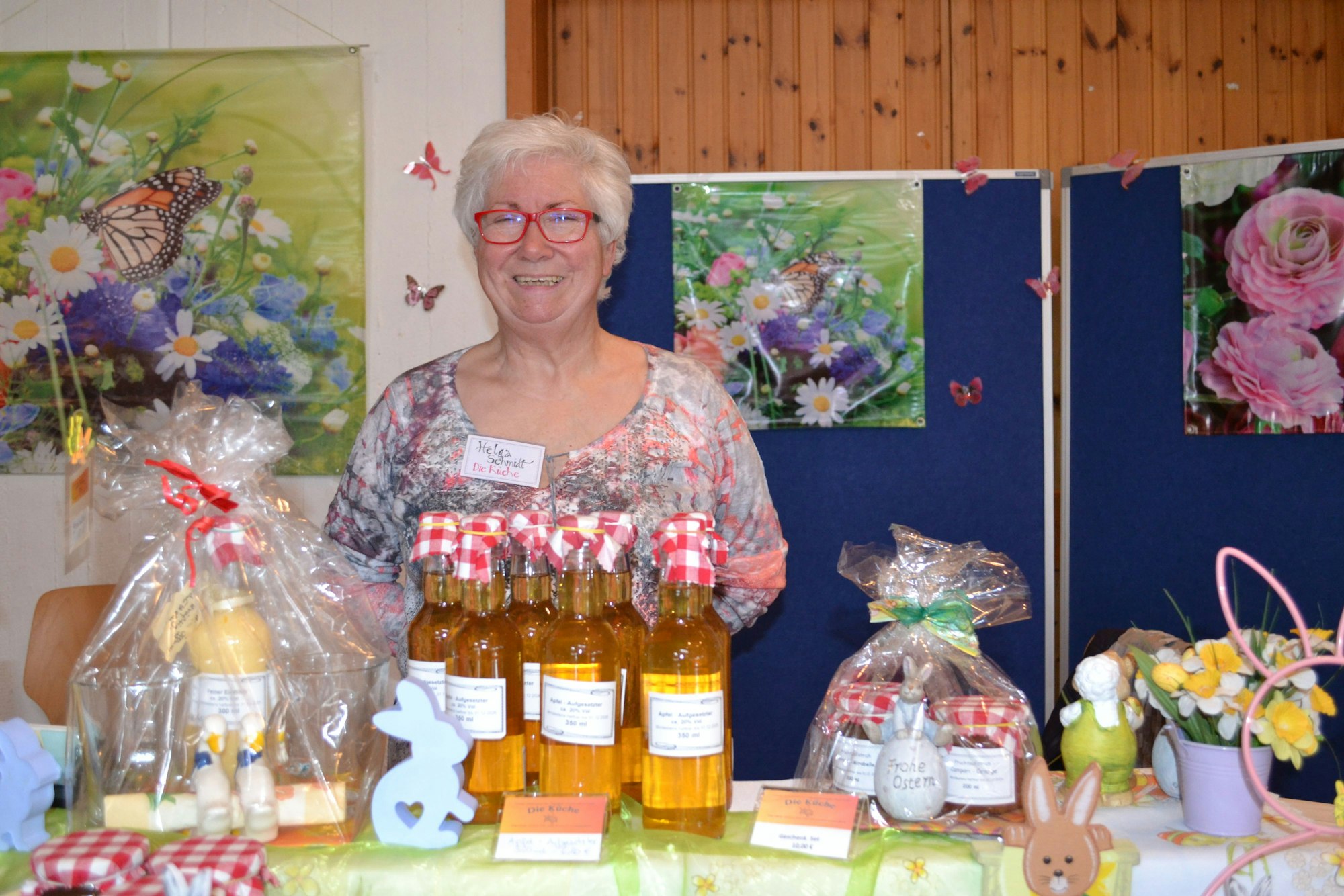 Eine Frau steht hinter einem Verkaufsstand. Sie bietet Getränke und Marmeladen an.