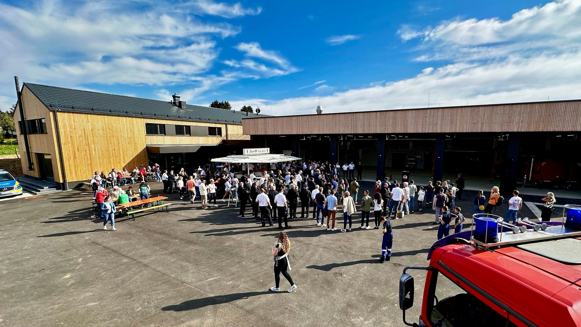 Ein modernes Gebäude mit einer holzverkleideten Fassade; im Hof stehen Menschen und ein Feuerwehrfahrzeug.