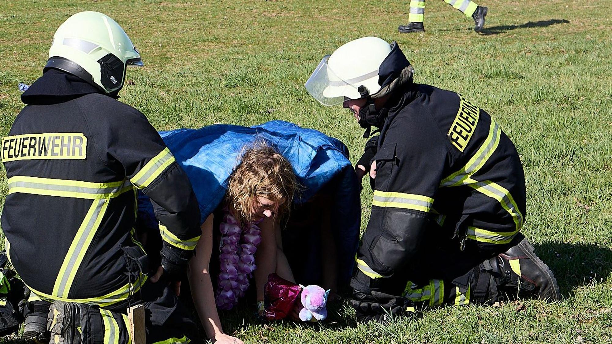 Zwei Feuerwehrleute knien im Rahmen einer Übung bei Verletztendarstellern, die sich eine Decke über den Kopf gezogen haben und über eine Wiese krabbeln.