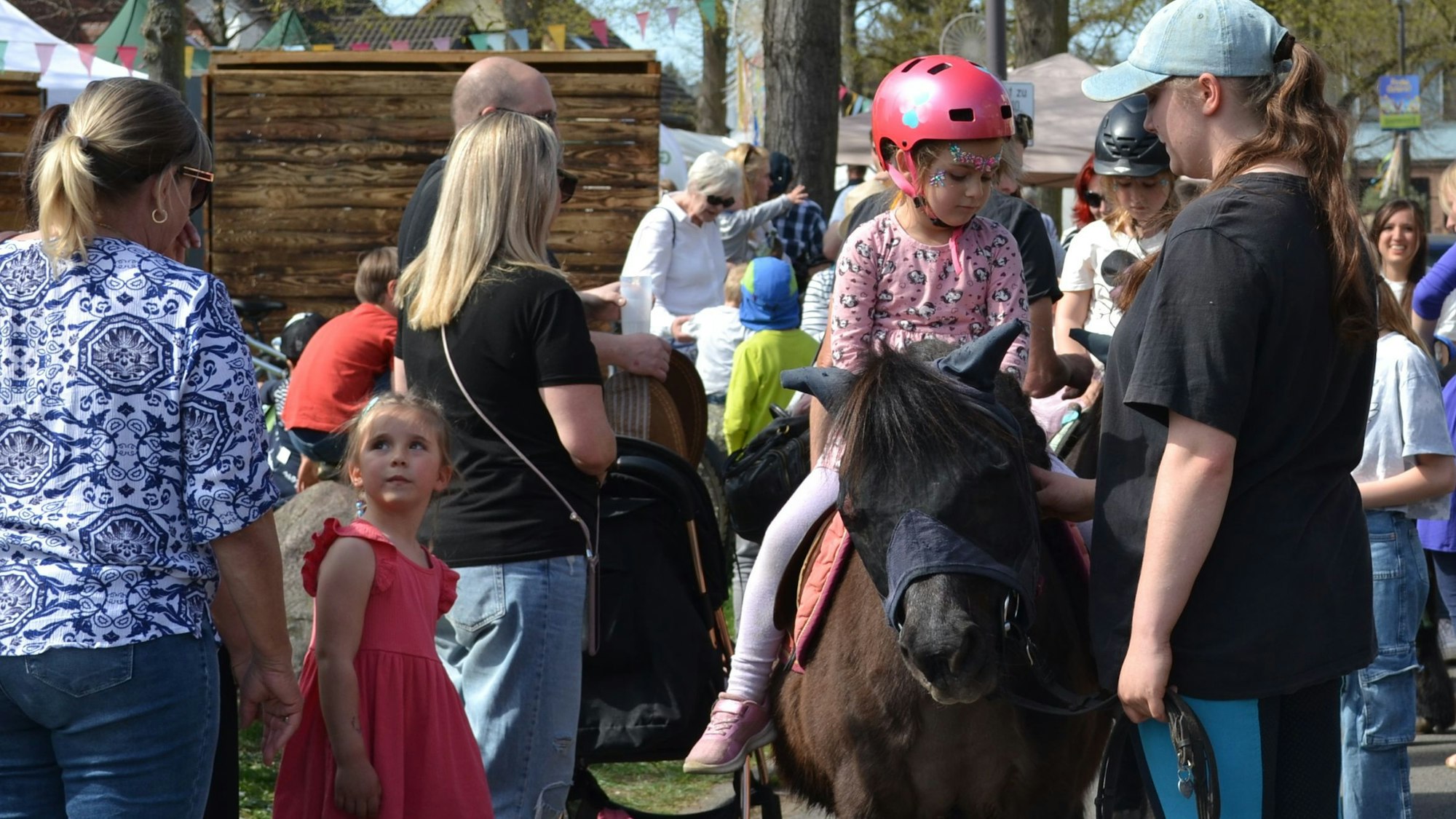 Ein kleines Mädchen sitzt auf einem Pony; andere Kinder warten ebenfalls auf das Ponyreiten.